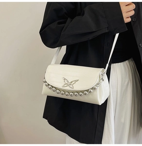Detail of white embossed leather crossbody bag with metal butterfly buckle and bead chain