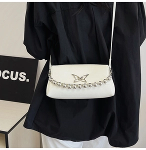 Close-up of white crossbody bag with silver butterfly emblem and large beaded chain