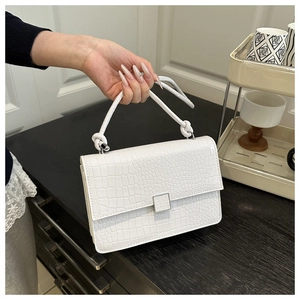 Detail of white crocodile pattern handbag with elegant knotted handle and silver metal clasp