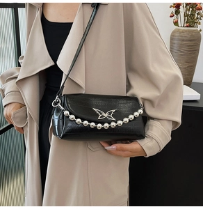 Detail of black embossed crossbody bag with silver butterfly emblem and beaded chain strap