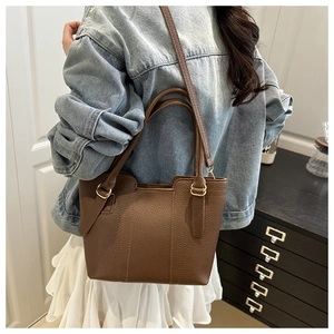 Detail of dark brown lychee leather tote bag with gold metal buckles and dual straps