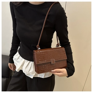 Detail of dark brown crocodile pattern faux leather handbag with metal buckle and shoulder strap