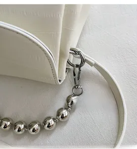 Close-up of silver metal hook and beaded decorative strap on white embossed handbag