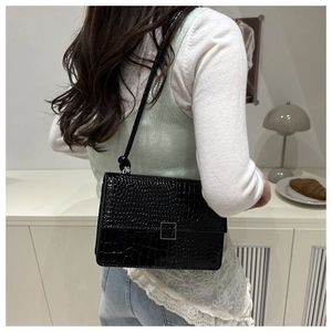 Detail of black crocodile texture handbag with silver buckle worn as a shoulder bag