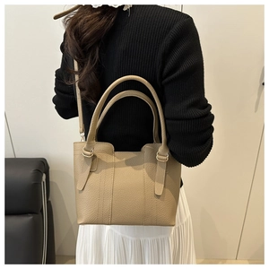 Close-up of beige lychee-patterned bucket bag with gold hardware worn by a model