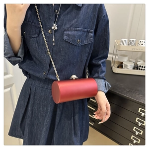 Détail d'une pochette cylindrique en satin rouge avec chaîne dorée et fermoir perle