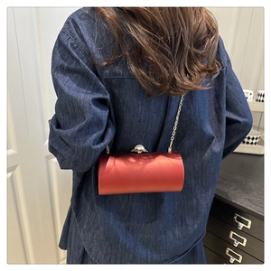 Détail du sac de soirée cylindrique en satin rouge avec fermoir perle et chaîne dorée