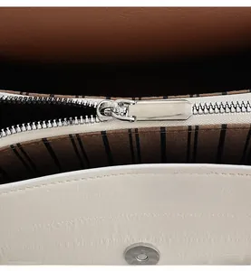 Detail of silver smooth zipper and striped lining inside the white crossbody bag