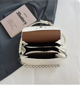 Detail view of the multi-layer interior compartments and silver beaded chain on a white bag
