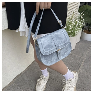 Detail of light blue vintage saddle bag with distressed texture and gold buckle