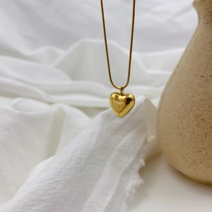 Polished gold heart pendant on a thin snake chain against an elegant neutral backdrop