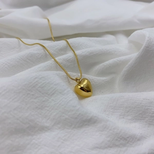 Elegant gold heart pendant necklace on a minimalist white linen background