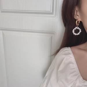 Close-up of golden hoop earrings featuring a circle of small white pearls on a model