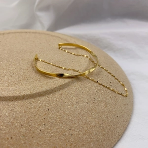 Macro detail of a gold twisted cuff bracelet with a delicate chain on a ceramic base