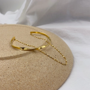 Close-up of gold twisted cuff bracelet with a delicate dainty chain on beige display