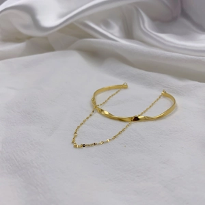 Detail of gold twisted bangle with delicate chain on soft white silk background