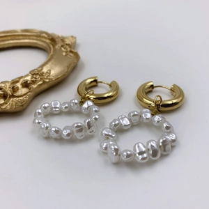 Detail of gold hoops with baroque pearl pendants next to a vintage frame