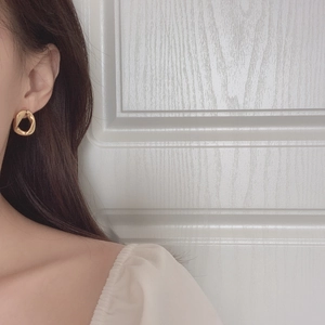 Minimalist irregular geometric gold earrings worn by a model against a neutral background
