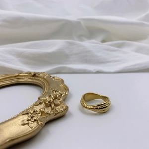 Minimalistischer goldener Gliederring mit geflochtenem Rand auf weißem Stoff