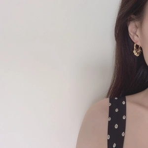 Detailed view of gold hoop earrings with hanging metal discs on a model's ear