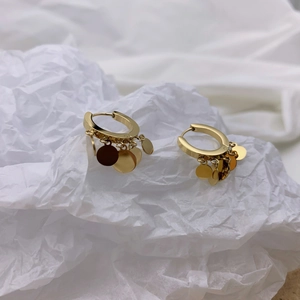 Detailed close-up of golden hoop earrings with round sequins on white paper background
