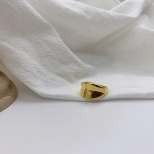 Detail of a minimalist gold irregular concave ring on a white textured fabric surface