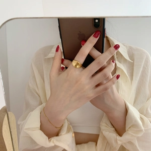 Macro detail of glossy gold wide irregular ring and delicate chain bracelet on hand