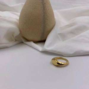Polished gold signet ring on white fabric, minimalist oval design with high-gloss finish