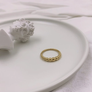 Primo piano artistico di un anello a sfere dorate minimalista su un piatto di ceramica bianca