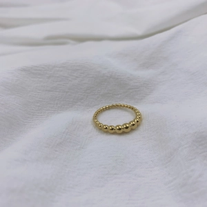 Anello con sfere dorate minimalista con perle sfumate su sfondo di tessuto bianco