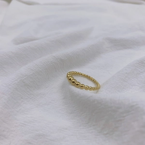 Anello minimalista con perline dorate e design a gradiente su sfondo in tessuto