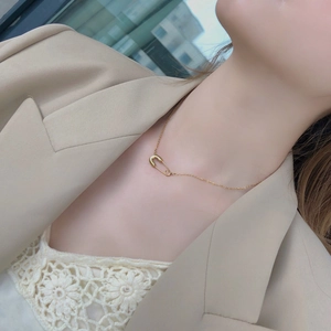 Collana minimalista dorata a spilla da balia indossata con un elegante blazer beige
