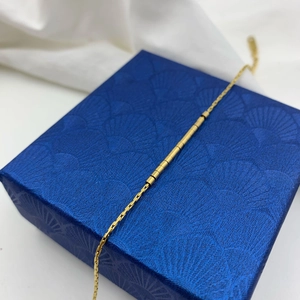 Détail d'un bracelet chaîne en or avec segments cylindriques sur boîte bleue