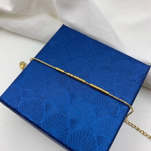 Détail d'un bracelet chaîne doré minimaliste avec perles cylindriques sur boîte bleue