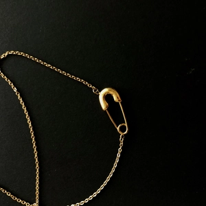 Macro di una collana dorata con ciondolo a spilla da balia minimalista e catena fine