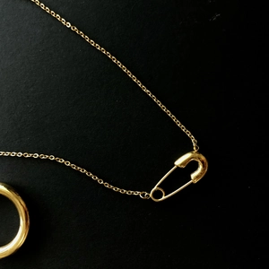 Collana con spilla da balia dorata minimalista e set di anelli lucidi su nero