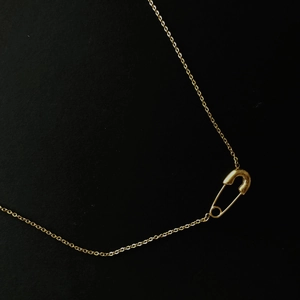 Collana minimalista con spilla da balia dorata su sfondo nero con finitura lucida