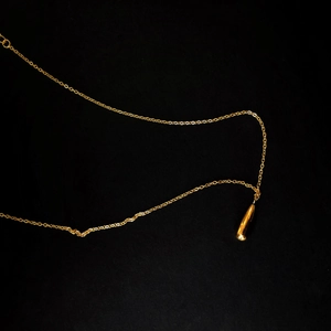 Detailed view of polished golden bullet-shaped pendant on a minimalist chain necklace