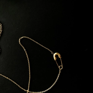 Macro di una collana con ciondolo a spilla da balia dorata su sfondo nero profondo