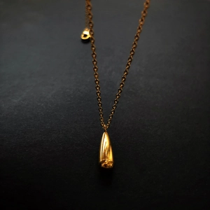 Macro shot of a polished gold teardrop pendant necklace on a sleek black background