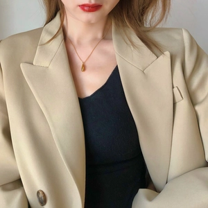 Close-up of a minimalist gold teardrop pendant necklace worn over a beige suit