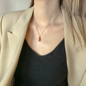 Close-up of golden teardrop pendant necklace worn with professional beige blazer outfit