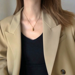 Close-up of a glossy gold teardrop pendant necklace worn with a chic beige blazer
