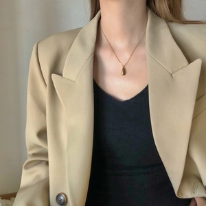 Close-up of minimalist gold teardrop pendant necklace worn by a model in professional attire
