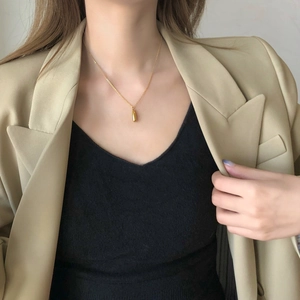 Polished gold teardrop pendant necklace layered over a beige blazer for elegant office style