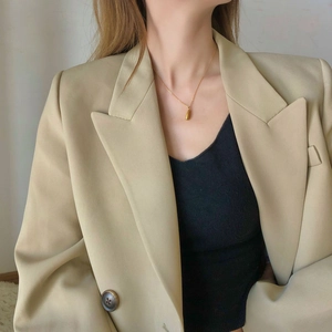 Close-up of a gold teardrop pendant necklace worn with a chic beige blazer outfit
