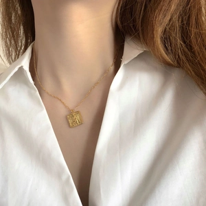 Détail d'un pendentif carré en or 18K gravé d'un ange sur une chaîne maille trombone