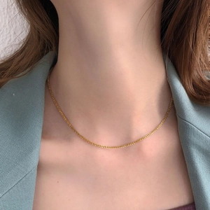 Minimalist gold thin chain necklace worn at the collarbone over a light blue blazer