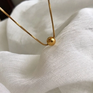 Minimalist gold round bead pendant necklace on a delicate box chain over white fabric