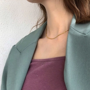 Close-up of elegant gold cylinder-link chain necklace on model wearing a blazer